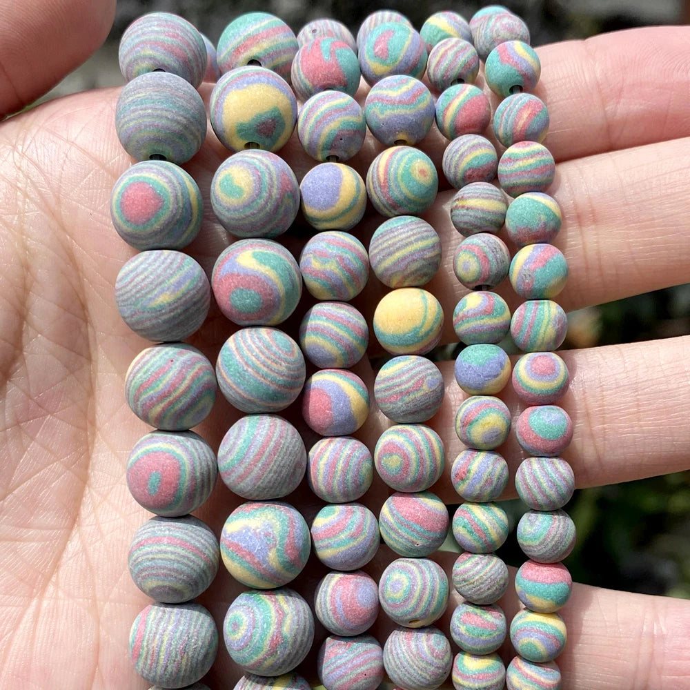 A close-up of a hand holding multiple strands of round marbled beads in pastel colors, including pink, yellow, blue, green, and purple swirls on a gray base.