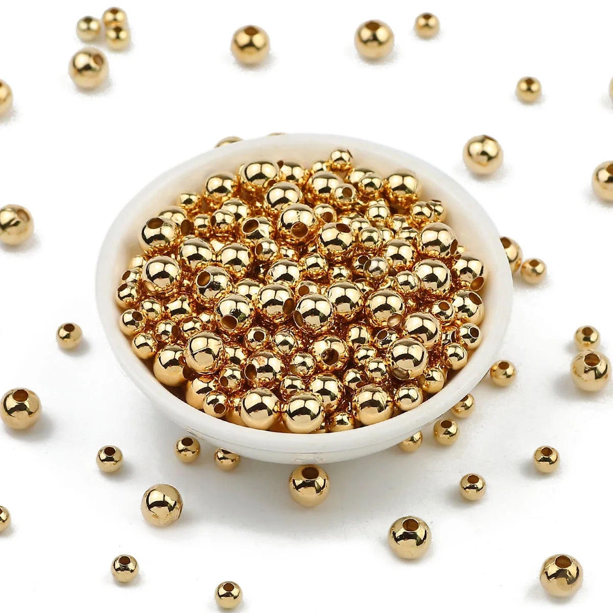 Gold beads in a white bowl with scattered beads on a white background