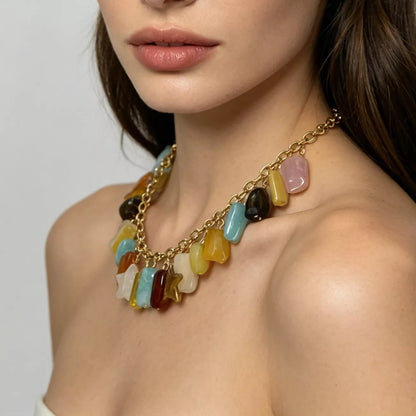 A close-up of a model wearing a gold chain bohemian necklace adorned with colorful, irregular stone-like charms in yellow, blue, pink, brown, and white.