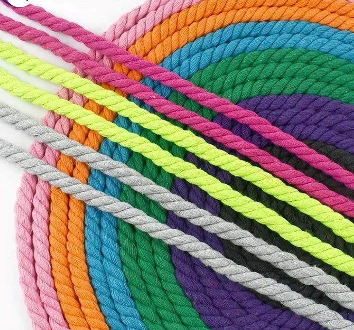 A close-up of twisted macrame rope cords arranged in overlapping diagonal and curved rows, showing multiple bright colors including pink, orange, yellow-green, blue, green, purple, black, and gray on a white background.