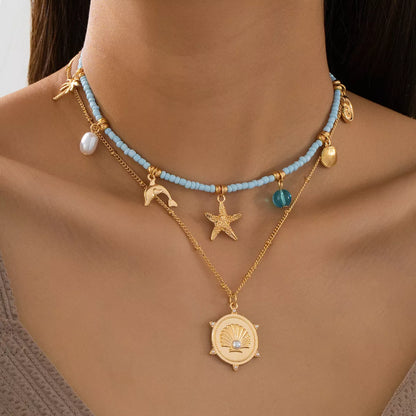 Necklace with blue beads, gold chain, and starfish pendant on a person's neck.