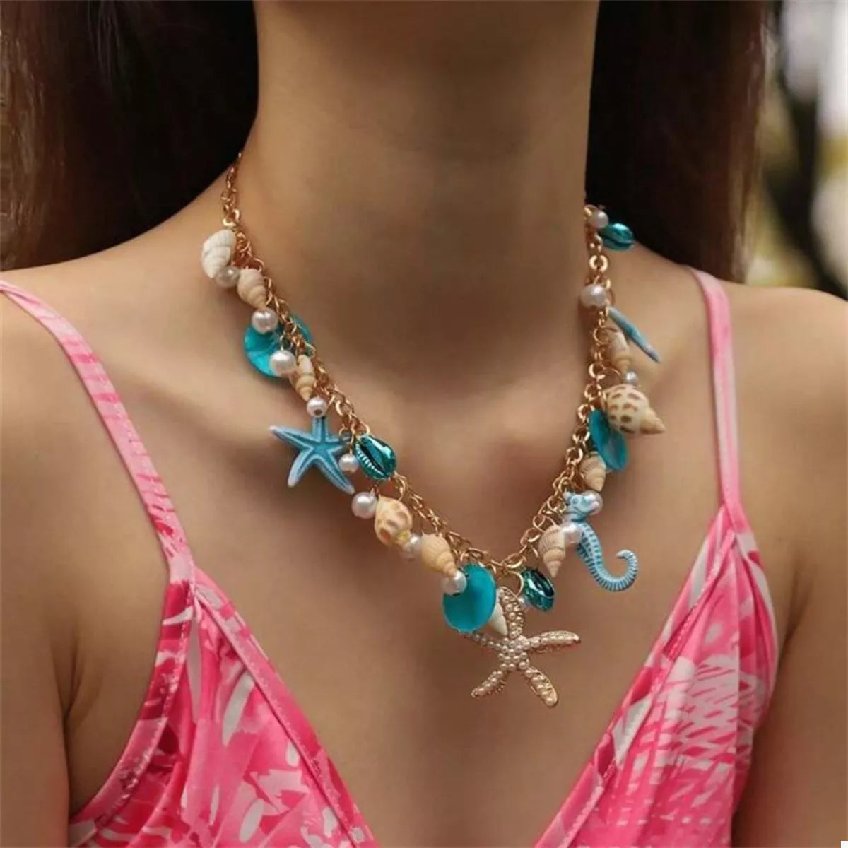 Necklace with seashell and starfish charms worn by a person in a pink top.