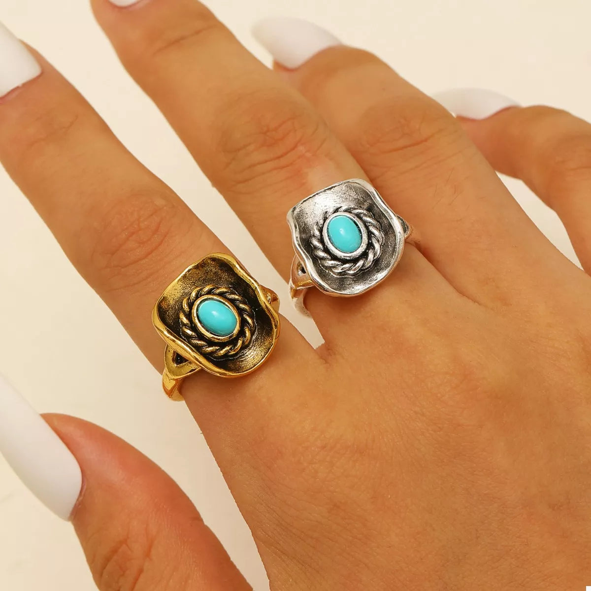 Two cowboy hat rings with turquoise stones on a hand against a neutral background