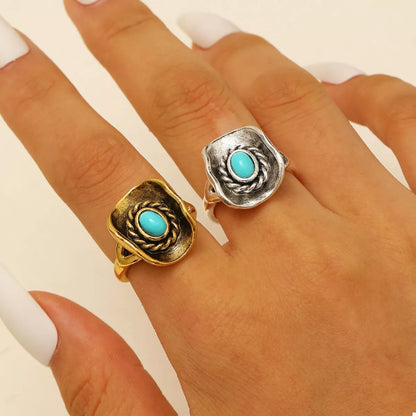 Two cowboy hat rings with turquoise stones on a hand against a neutral background