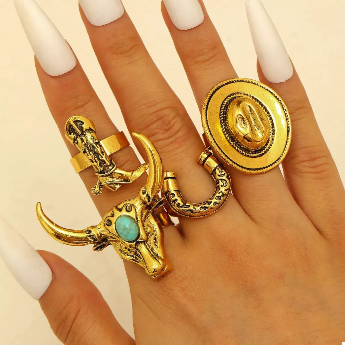 Gold western rings with bull skull design on a hand against a beige background