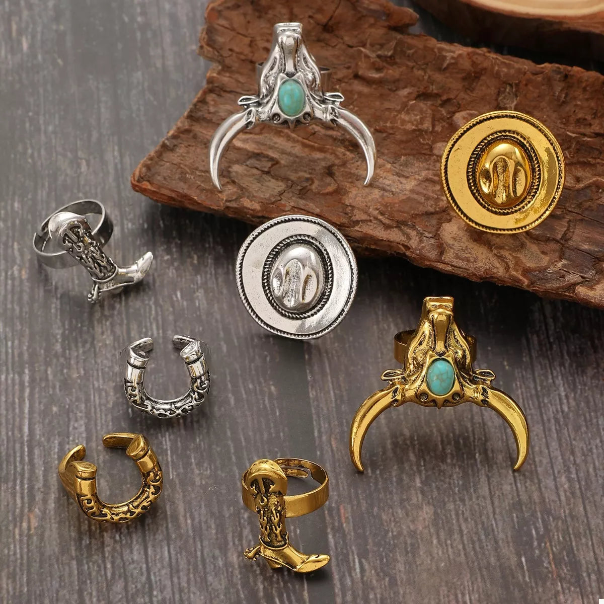 Collection of various western cowboy jewelry pieces including rings and pendants on a wooden surface.