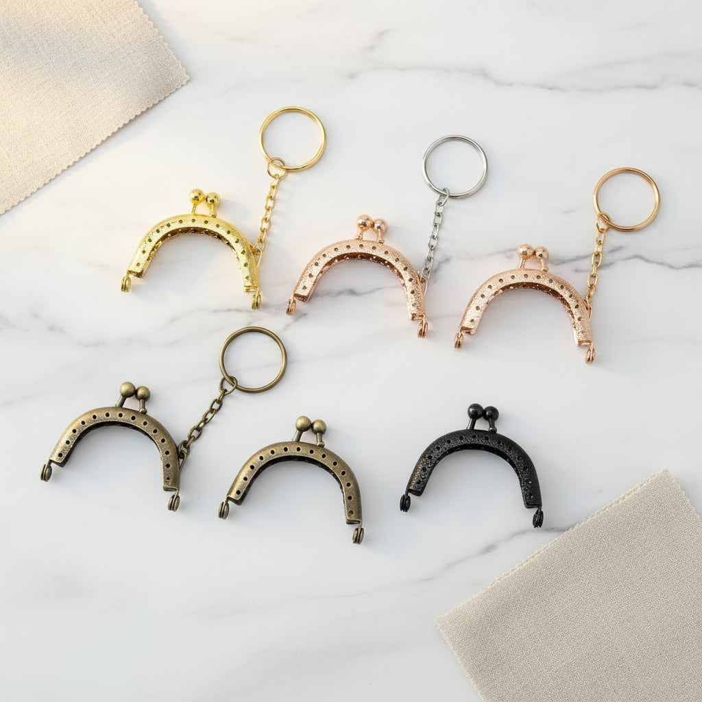 Six antique-style kiss-lock coin purse keychains in different metal finishes (gold, silver, rose gold, bronze, and black) arranged on a plain white background.