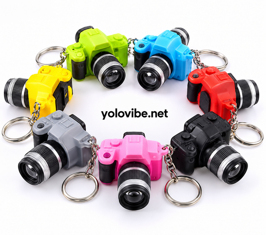 Miniature toy camera keychains in assorted colors (green, blue, red, black, gray, pink) arranged in a circle, each with a silver metal key ring and chain, on a white background with 'yolovibe.net' text in the center.