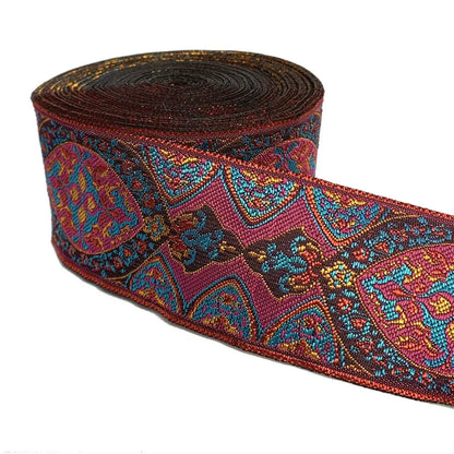 A roll of decorative embroidered ribbon with a detailed paisley and floral pattern in red, blue, gold, and brown on a white background.