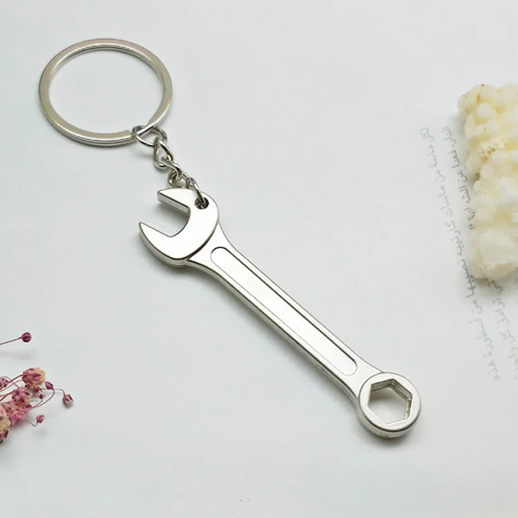 Silver wrench-shaped keychain on a light gray background with floral elements.