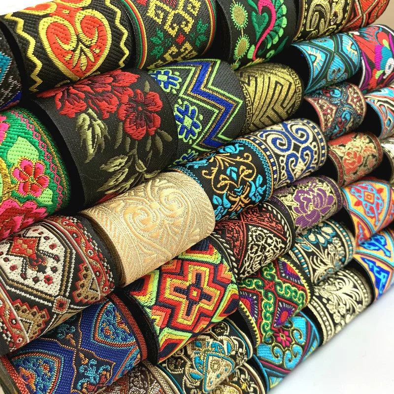 A close-up stack of rolled embroidered ribbons with intricate geometric and floral patterns in many colors, including black, red, blue, green, gold, and beige.