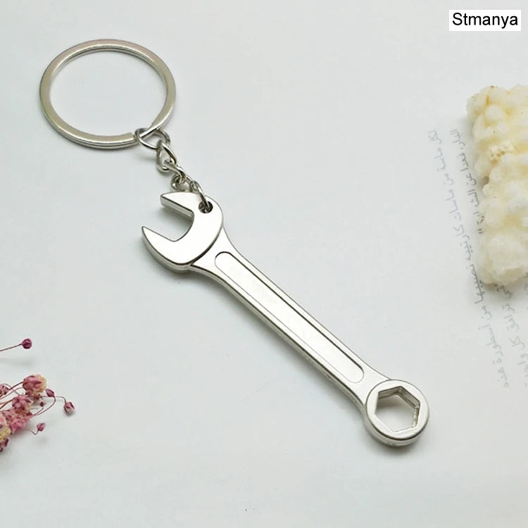 Silver wrench keychain on a light gray background with floral elements.