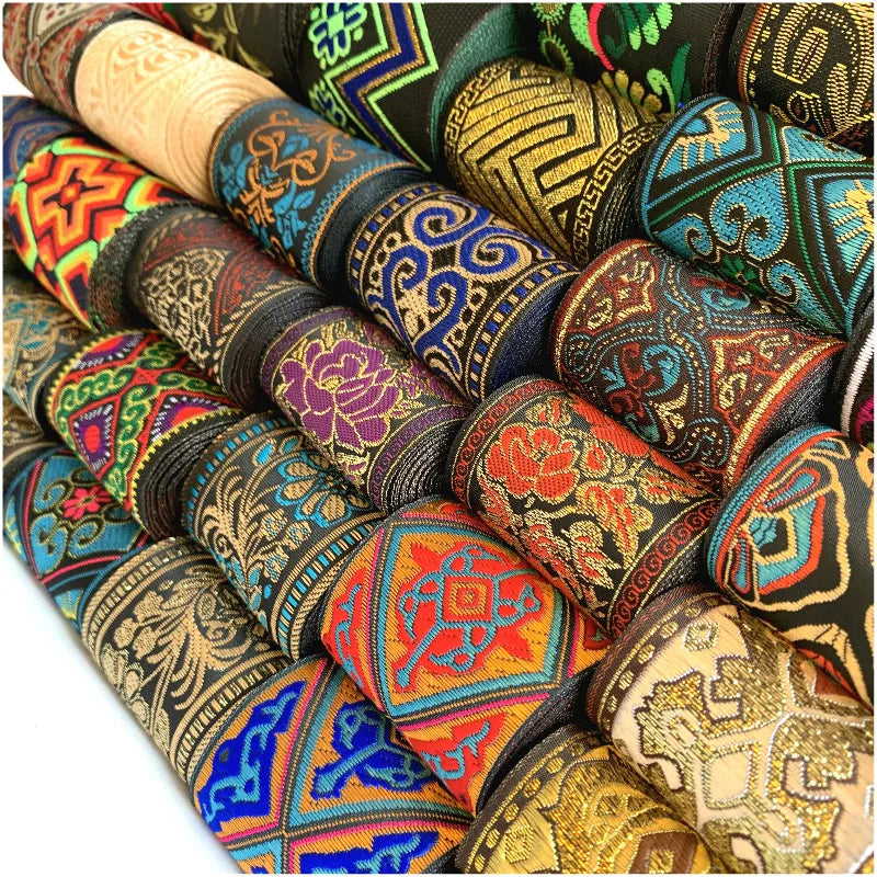 A close-up arrangement of multiple rolled and folded patterned fabric strips showing intricate traditional-style embroidery and woven motifs in many colors.