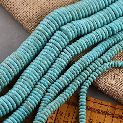 Turquoise round disc beads arranged in parallel strands on a burlap and bamboo mat background.