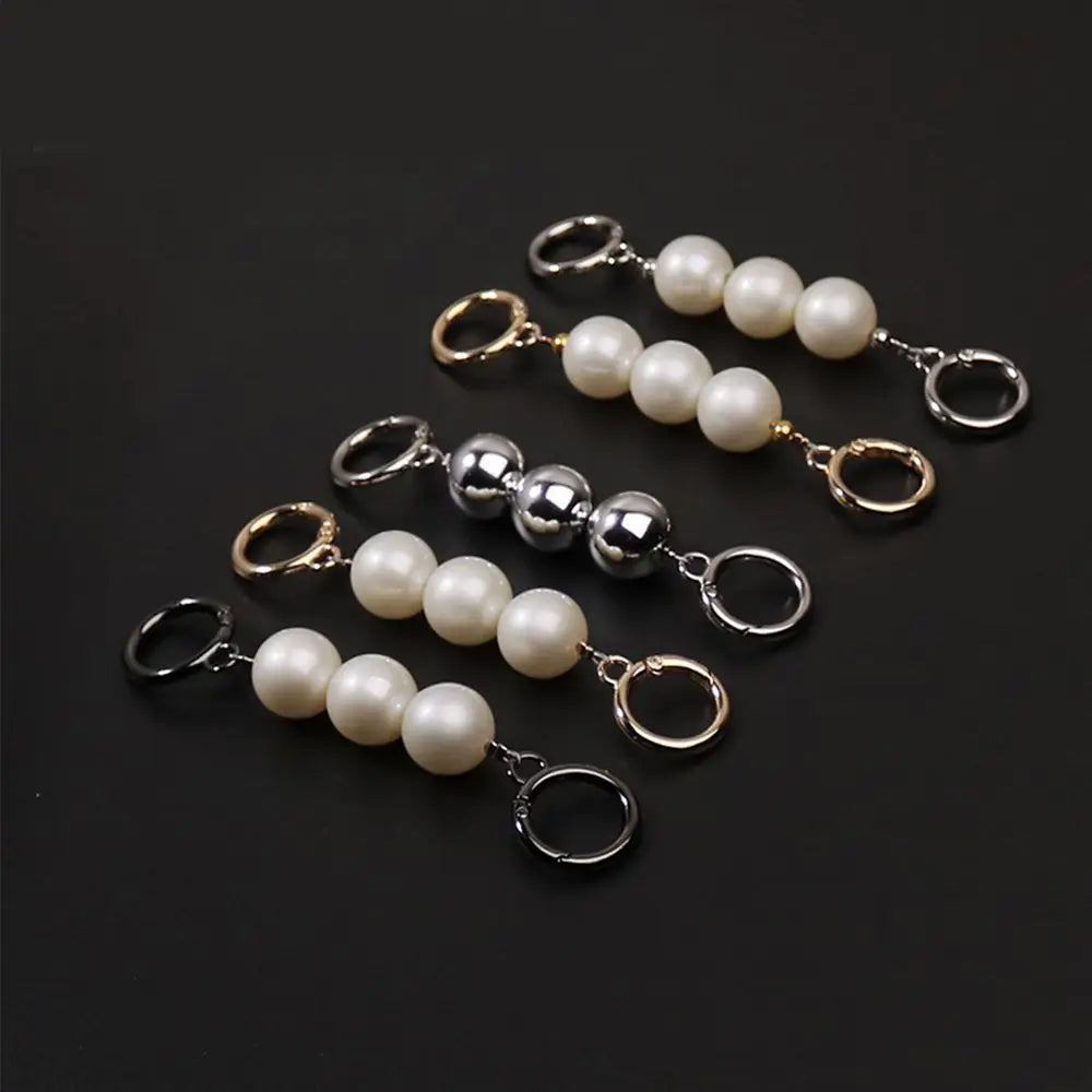 Pearl keychain clips purse extender with gold, silver, and black metal loops on a dark background