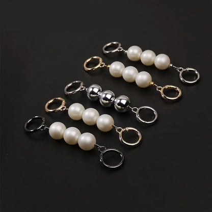 Pearl keychain clips purse extender with gold, silver, and black metal loops on a dark background