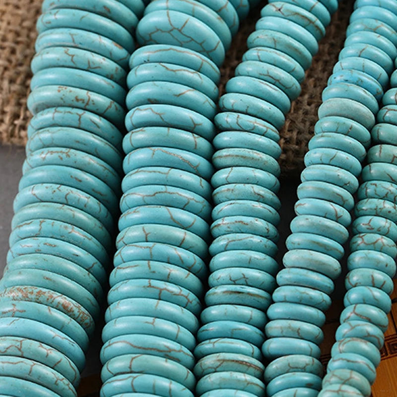 Close-up of multiple strands of turquoise-colored round beads with natural matrix cracks, arranged vertically on a textured brown surface.