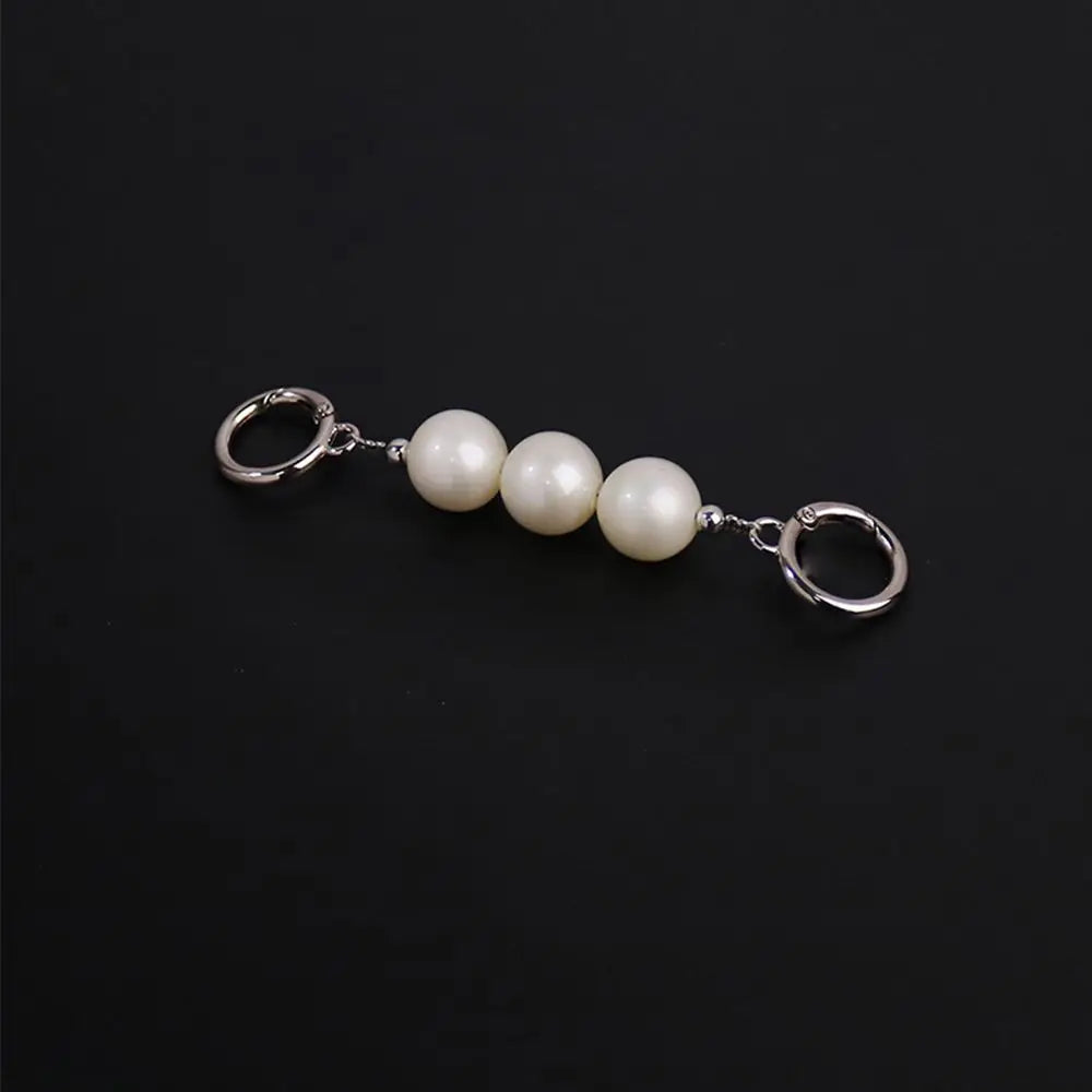 A silver-tone keychain featuring three smooth, lustrous white pearl beads connected by small silver links and flanked by two lobster claw rings, set against a solid black background.
