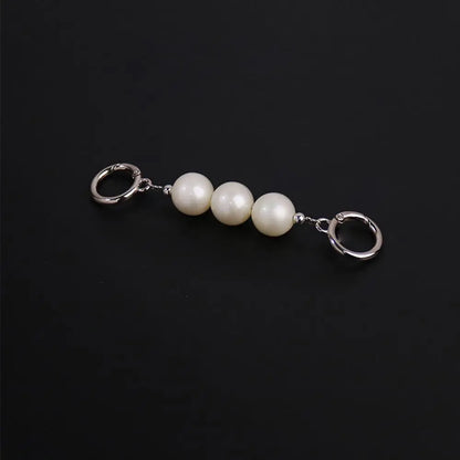 A silver-tone keychain featuring three smooth, lustrous white pearl beads connected by small silver links and flanked by two lobster claw rings, set against a solid black background.