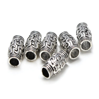 Six silver-toned cylindrical beads with intricate scrollwork patterns and ribbed ends, arranged on a plain white background.