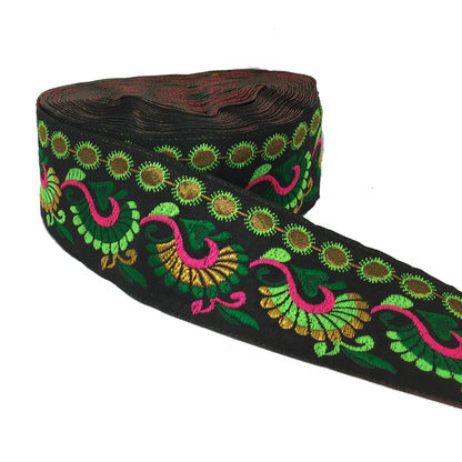 A roll of black decorative trim featuring colorful embroidered patterns of green, pink, and gold paisley and floral motifs, shown on a plain white background.