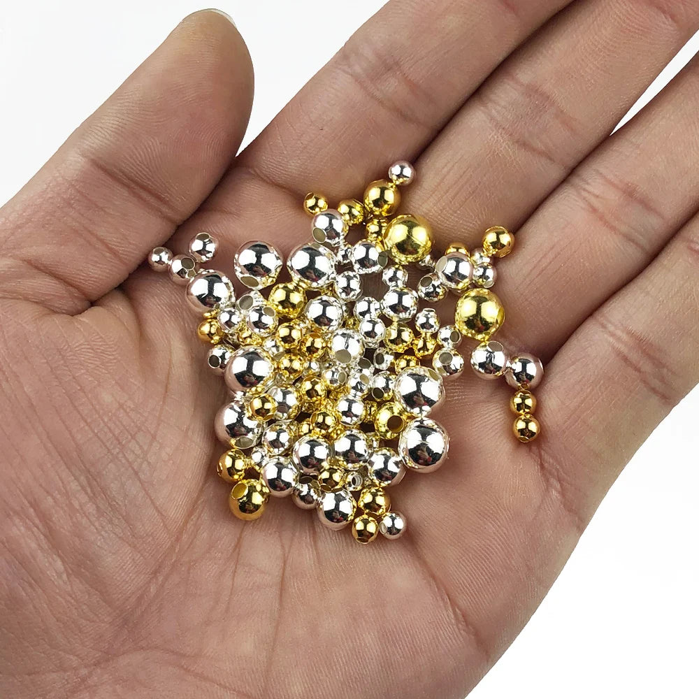 Hand holding a small pile of gold and silver metal balls on a white background