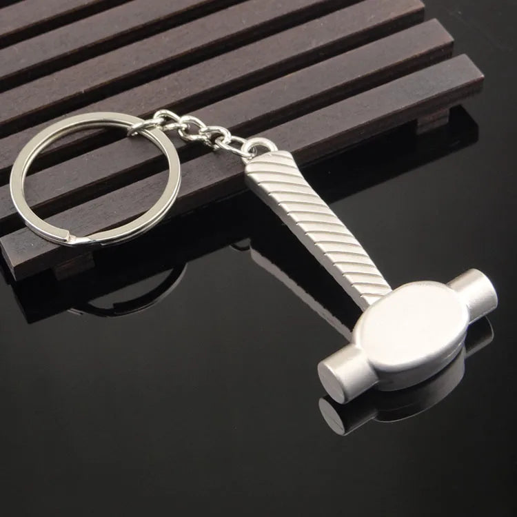 Metal keychain with a hammer design on a reflective black surface