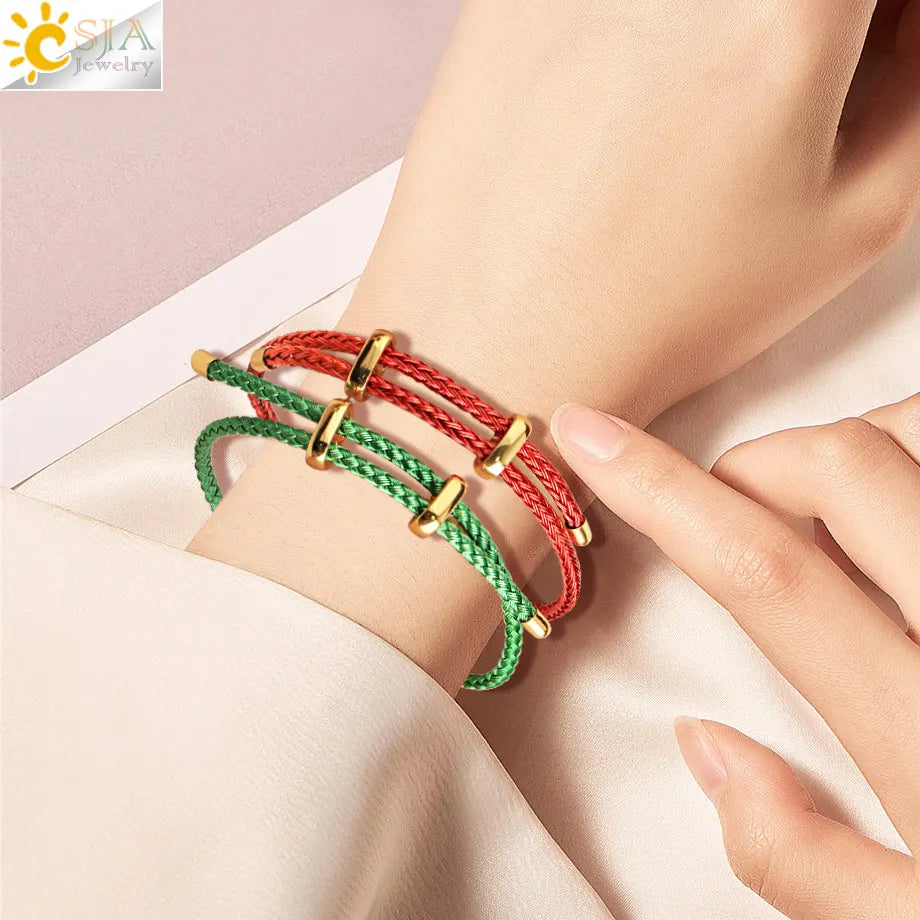Braided cord bracelets in red and green, with gold-toned toggle clasp details, shown worn on a person's wrist with a finger touching one bracelet.