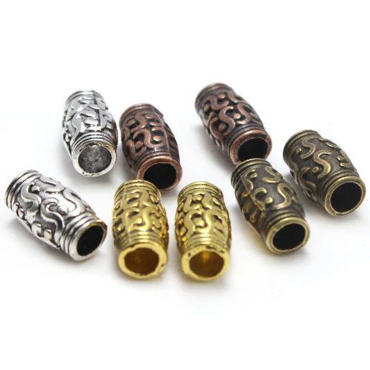 Nine ornate cylindrical metal spacers or beads in silver, bronze, and gold finishes, arranged on a plain white background.