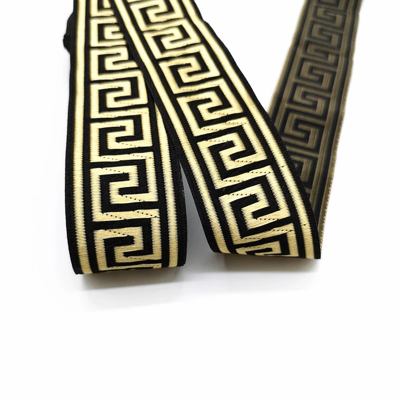 A close-up of a black and beige Greek key patterned ribbon, folded to show its texture and design on a white background.