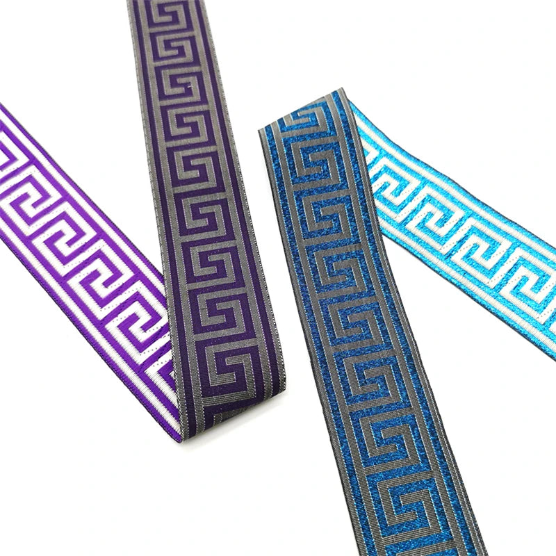 Three decorative Greek key or vintage bohemian trim ribbons in purple, blue, and light blue, arranged diagonally on a white background.