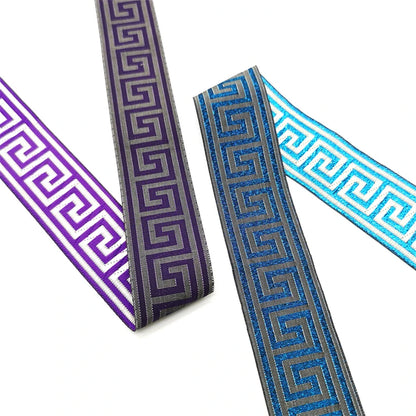 Three decorative Greek key or vintage bohemian trim ribbons in purple, blue, and light blue, arranged diagonally on a white background.