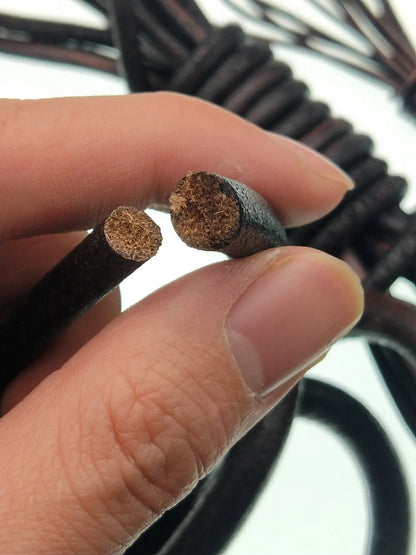 A close-up of a hand holding two ends of a black leather cord, showing the textured brown inner lining. More coiled cords are visible in the blurred background.