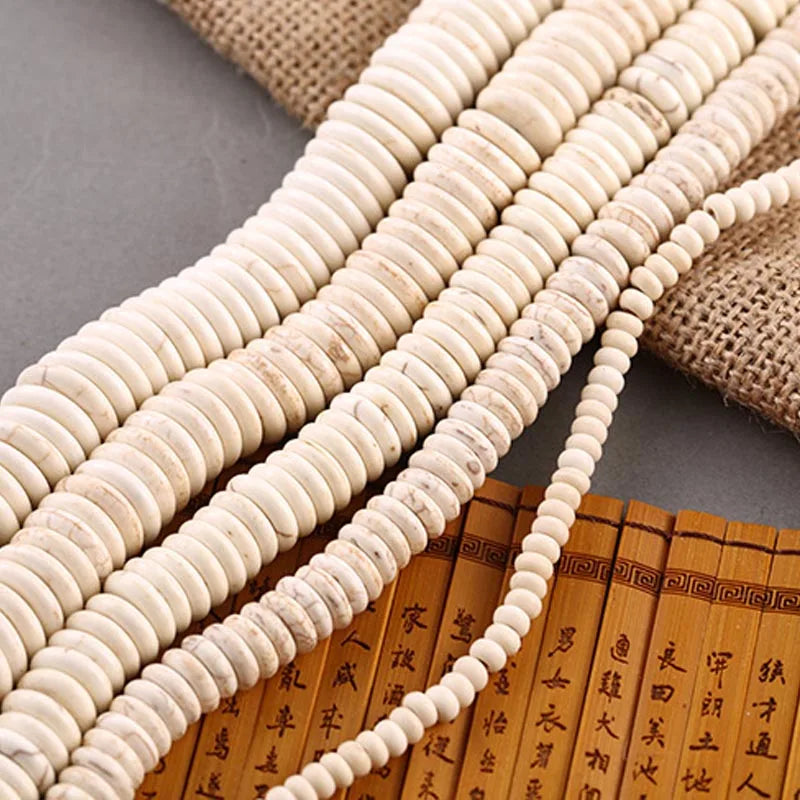 Multiple strands of small round off-white beads arranged diagonally over a brown burlap cloth and a yellow bamboo-style book with black calligraphy.