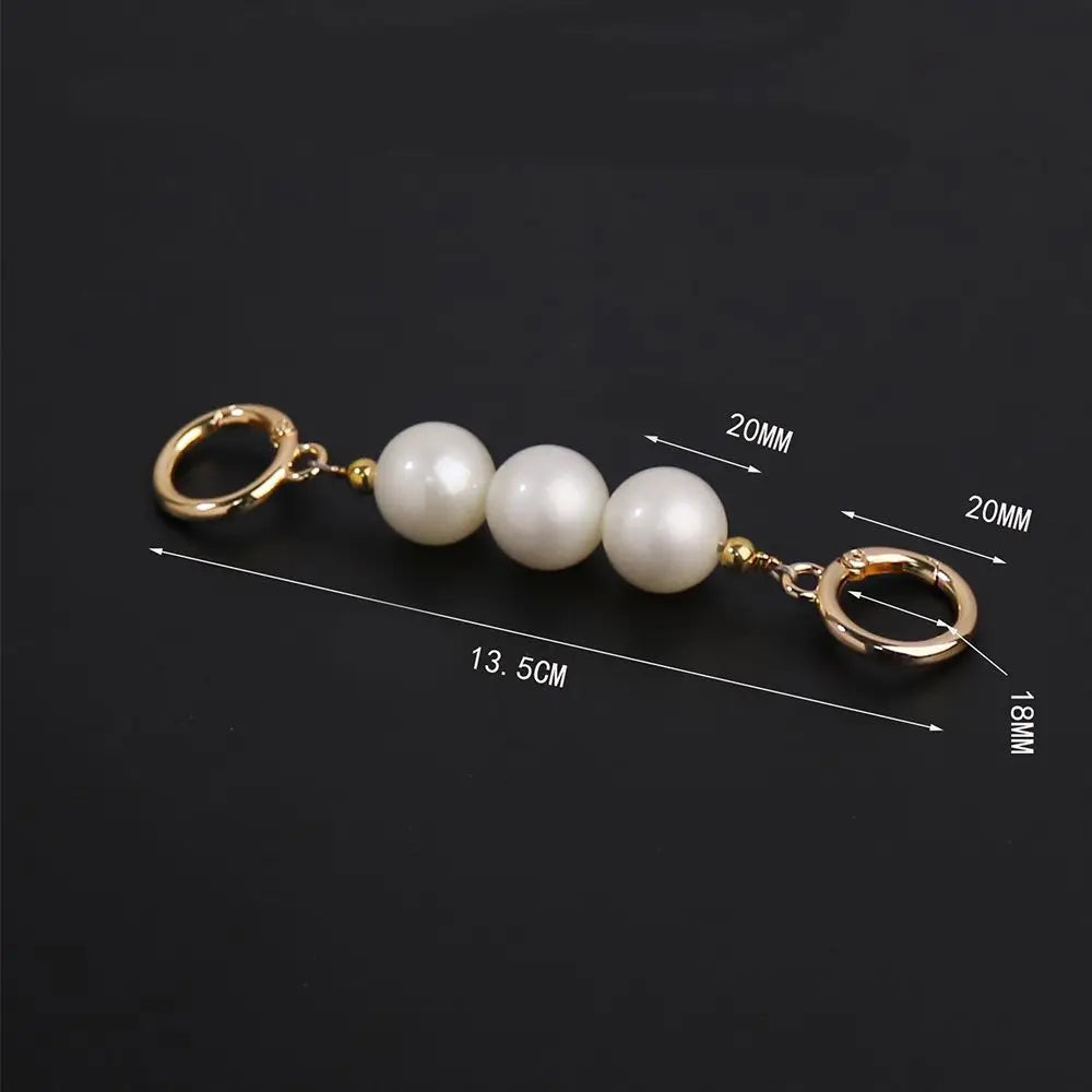 A keychain or bag charm with three white pearl-like beads and gold-tone metal rings, shown on a black background with overlaid dimension lines and measurements.