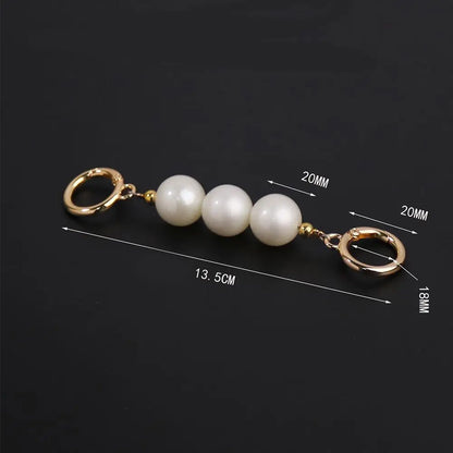 A keychain or bag charm with three white pearl-like beads and gold-tone metal rings, shown on a black background with overlaid dimension lines and measurements.
