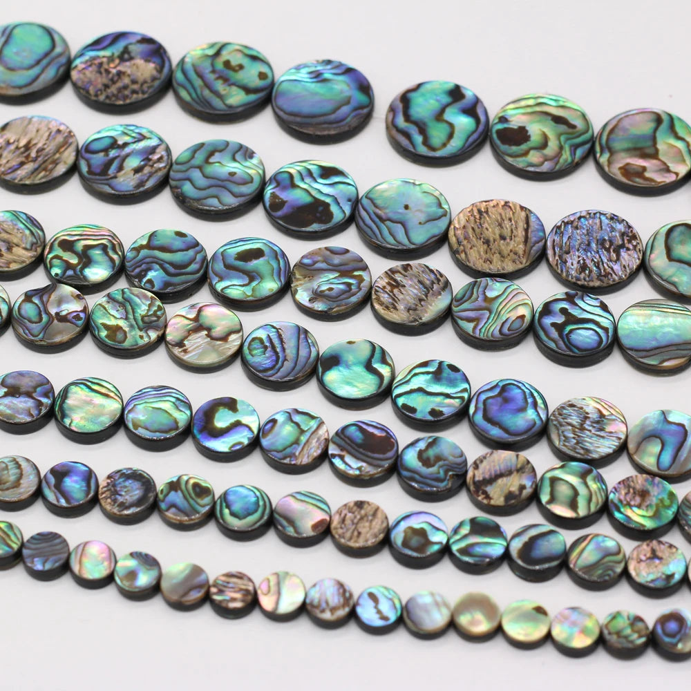 Multiple strands of round abalone shell beads with iridescent green, blue, purple, and brown marbled patterns, arranged on a plain white background.