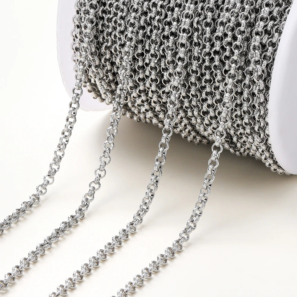 A close-up of a spool of silver metallic chain with several strands draped out onto a light neutral background.