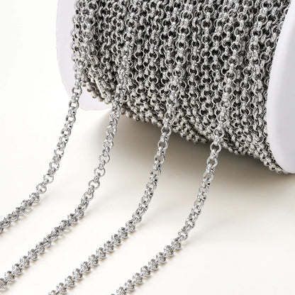 A close-up of a spool of silver metallic chain with several strands draped out onto a light neutral background.