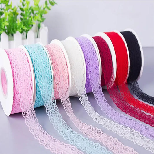 Six rolls of decorative lace trim in pink, light blue, pale pink, white, purple, red, and black, arranged diagonally with the lace strands draped out on a light gray surface.