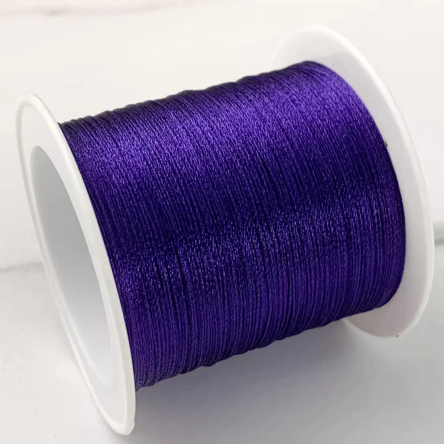 A close-up of a spool of vibrant purple embroidery thread wound tightly on a white plastic spool, set against a clean white background.