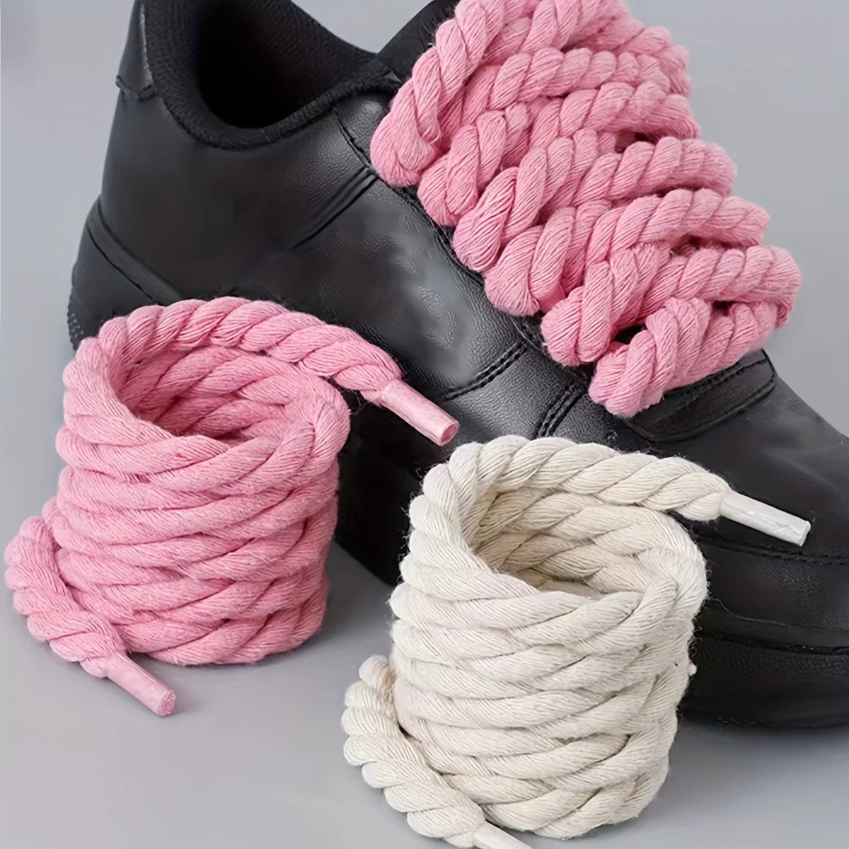 Black shoe with pink and white ropes on a gray background