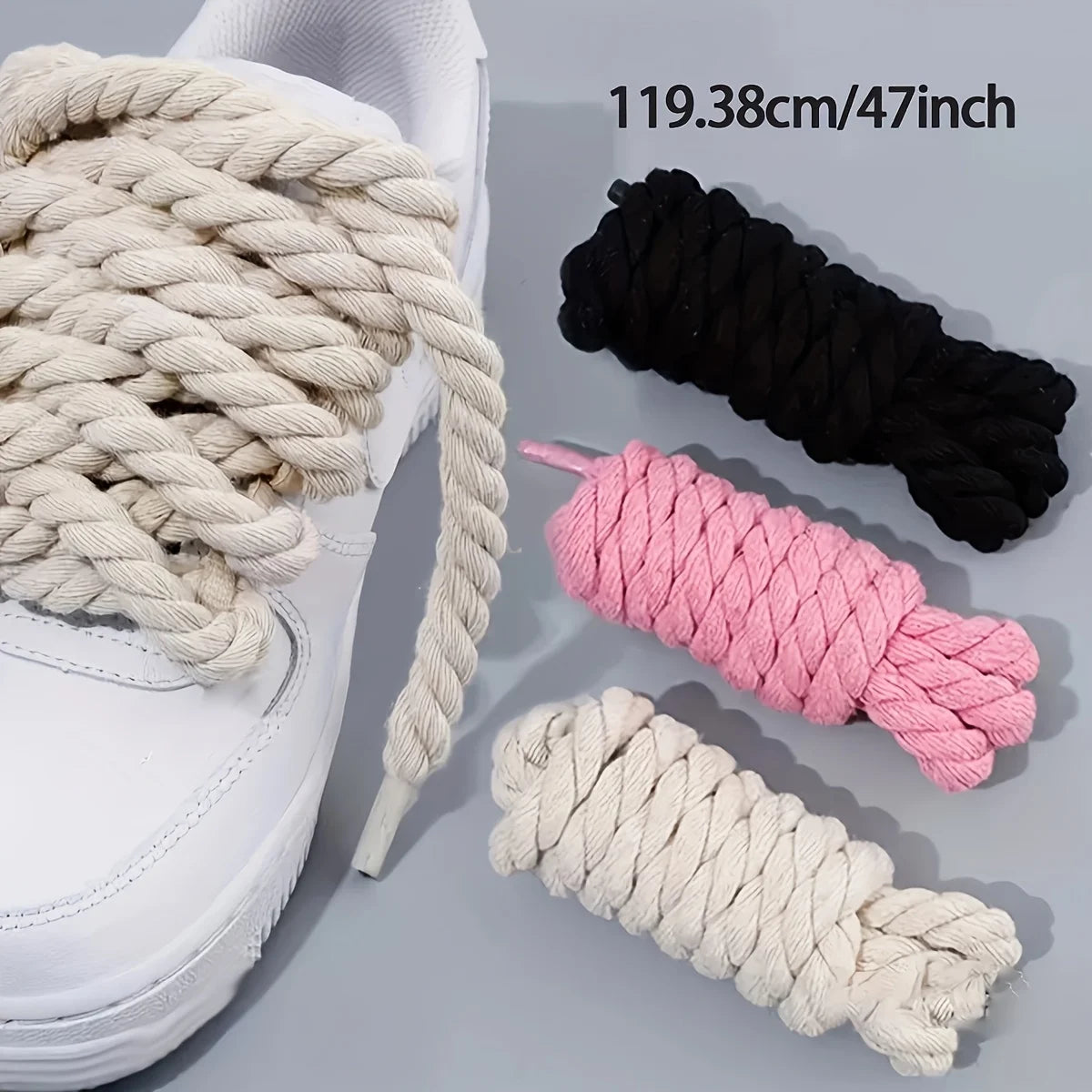 White sneakers with thick beige, black, and pink shoelaces on a light gray background.
