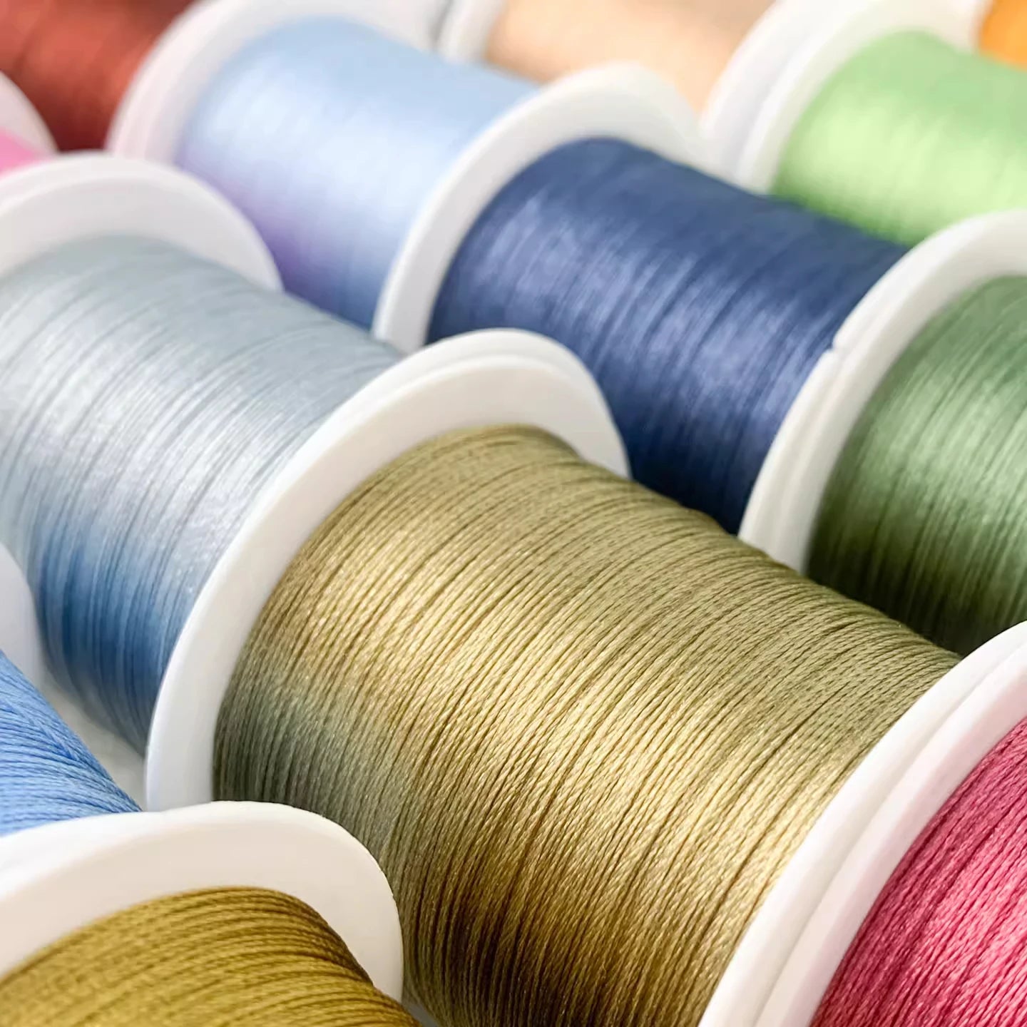 Close-up of multiple spools of thread or cord in assorted colors, including blue, green, pink, and gold, arranged diagonally.