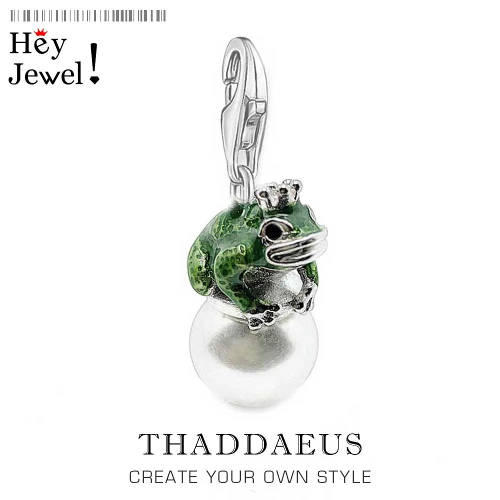 Jewelry pendant with green frog and pearl on a white background, branded 'Hey Jewel'.