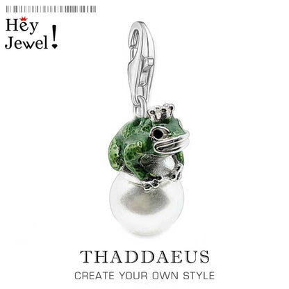 Jewelry pendant with green frog and pearl on a white background, branded 'Hey Jewel'.