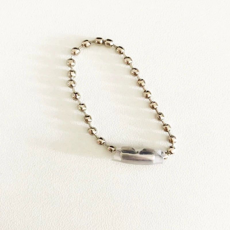 A silver-toned ball chain bracelet with a clear, faceted cylindrical bead centerpiece, displayed on a textured off-white background.