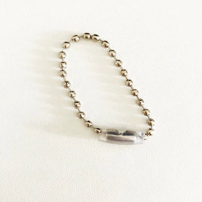A silver-toned ball chain bracelet with a clear, faceted cylindrical bead centerpiece, displayed on a textured off-white background.