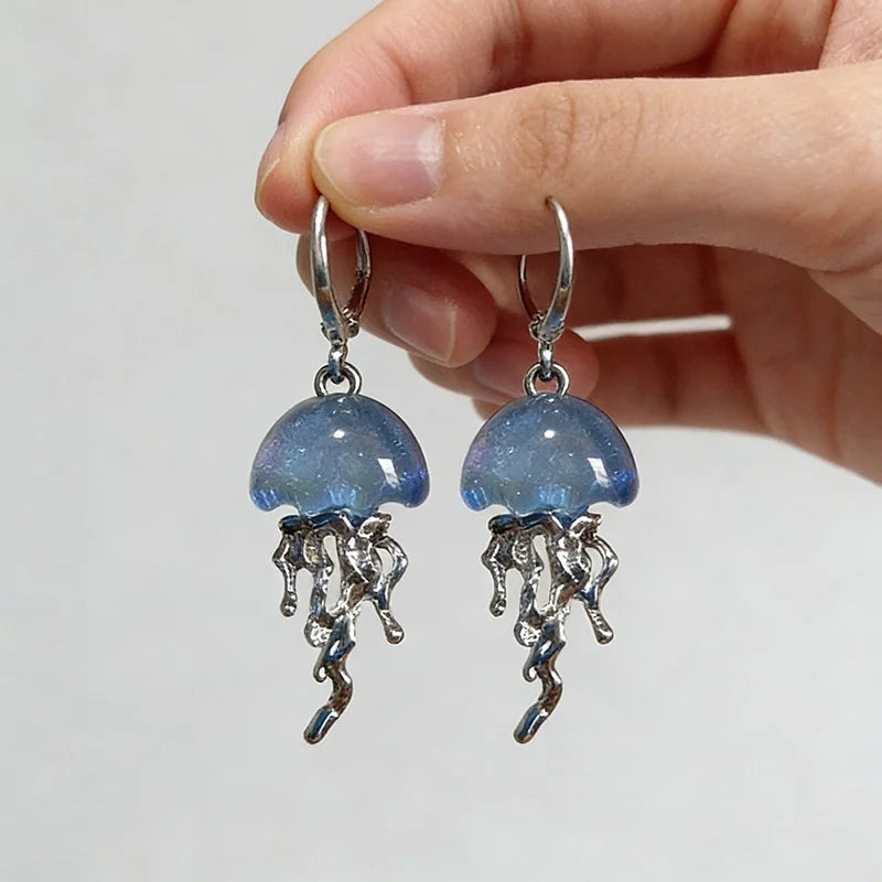 Jellyfish-shaped earrings held by a hand against a neutral background