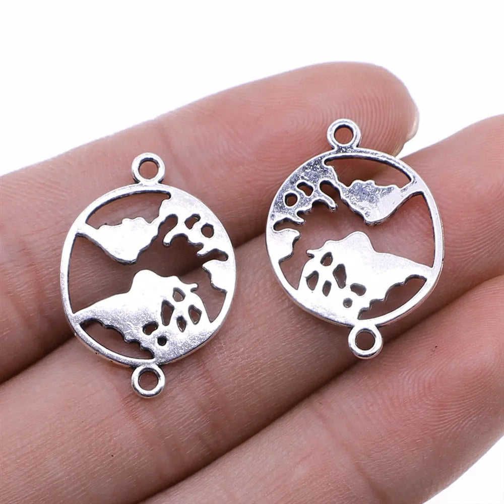 Two silver oval globe charms with cutout continents and loop attachments, shown resting on a person's fingers against a white background.